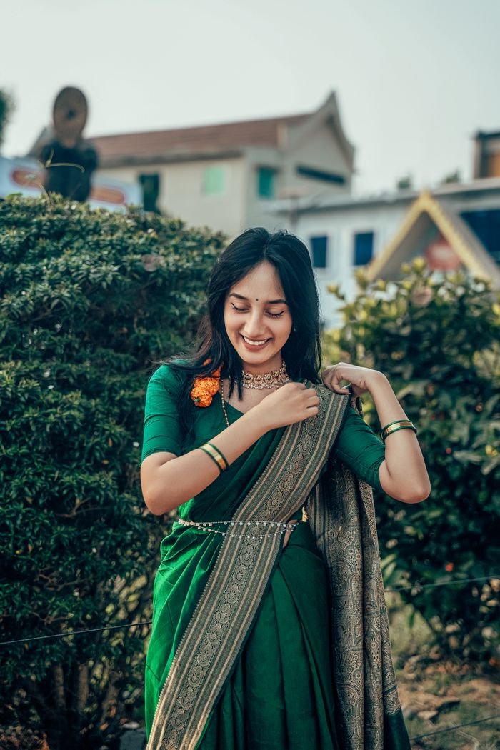 A beautifully captured portrait of a young woman in a traditional green saree amidst a lush outdoor setting.